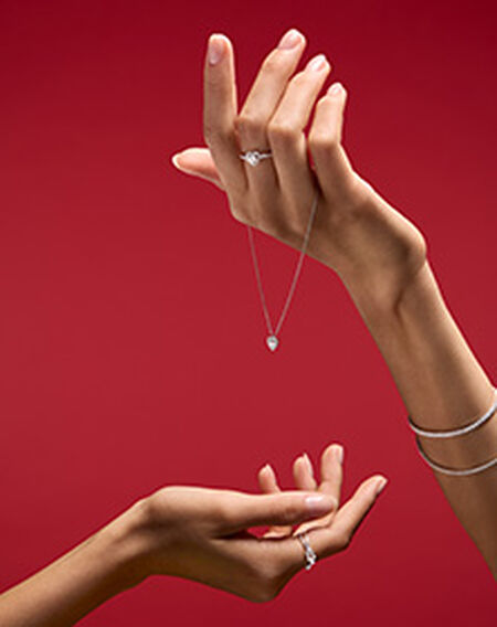 Une femme tenant des bijoux Maison Birks sur un fond rouge.